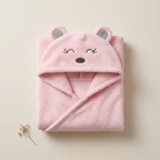 Pink hooded baby bath towel folded on cream linen with its animal-face hood visible.